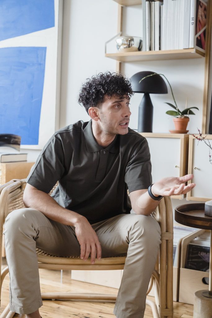 A Frustrated Man in Black Polo Shirt Talking while Sitting on a Chair.