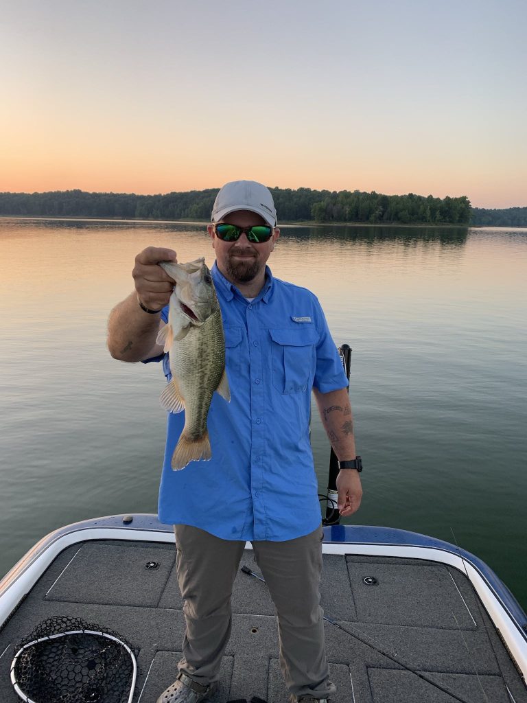 A Man in Blue Polo Shirt Holding a Fish while Standing on the Boat