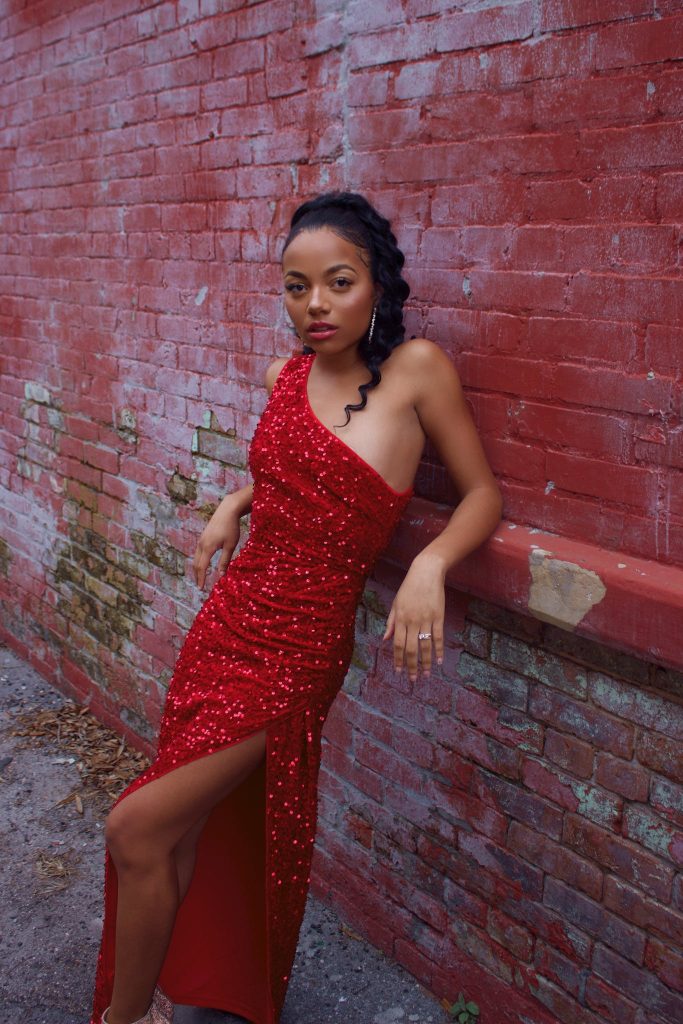 A Woman in Red Sequins Dress Leaning on Red Brick Wall while Looking at the Camera.