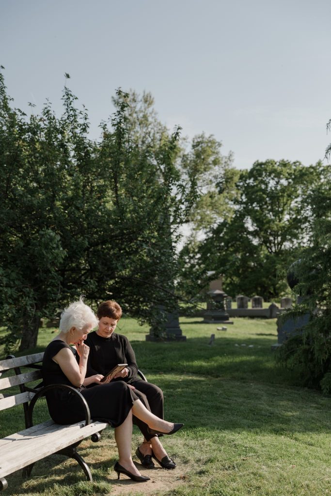 Women Sitting on a Bench Next to a Cemetery.